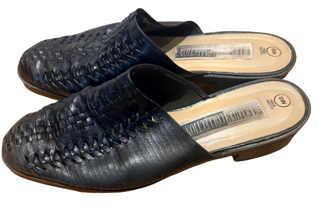 A pair of women's woven leather mule sandals in a black color, displayed against a plain white background.
